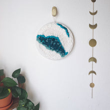 Load image into Gallery viewer, 12 &quot; round handcrafted woven wall hanging with teal, aqua, blue surrounded by creamy white fibers  hung from a brass hook.
