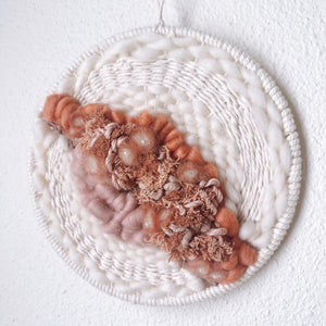 Close up of handcrafted round woven wall hanging with peach, coral and dusky rose, sand and cream wool and natural fibers