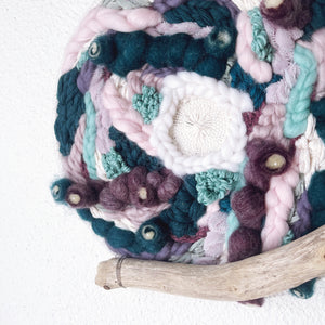 Close up of handcrafted 10" round woven wall hanging with lavender, mint, eggplant, teal and creamy white accented with driftwood 