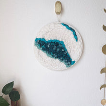 Load image into Gallery viewer, 12 &quot; round handcrafted woven wall hanging with teal, aqua, blue surrounded by creamy white fibers hung from a brass hook.
