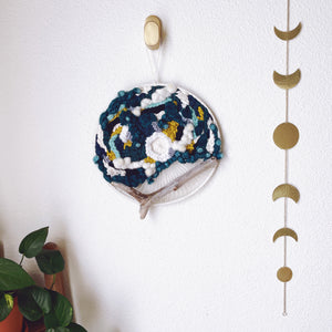 handcrafted 12" round wall hanging with teal, aqua, seafoam, navy, pistachio and creamy white natural fibers accented by driftwood from Oahu hung on a bronze hook